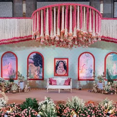 A grand and traditional stage for a South Indian half-saree function. The decor features massive floral chandeliers made of jasmine and pink flowers, with a custom backdrop depicting the stages of a woman's life.