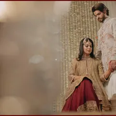 A regal and tender moment. The groom holds the bride's hand as she is seated, creating a portrait that feels both formal and deeply affectionate, set against a beautifully textured backdrop.