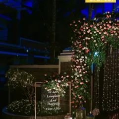 A romantic corner detail. A simple sign with the words "To Love, Laughter And Happily Ever After" is surrounded by soft florals, lanterns, and fairy lights.