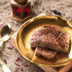 A close-up of the Coffee Crème Shahi Tukda, showing the coffee powder dusted on top and the creamy texture of the dessert.