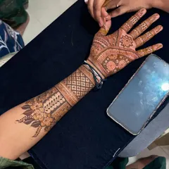 A close up of a detailed bridal mehendi application in progress. You can see the reference design on the phone, showing how I work with clients to bring their desired patterns to life with precision.