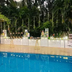 A stunning poolside setup for a 75th anniversary. The clean white food counters are decorated with flowers and fairy lights, reflecting beautifully in the water for an elegant evening celebration.