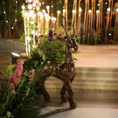 A whimsical decor element featuring a wooden deer statue adorned with fresh flowers. This piece adds a touch of enchanted forest magic to the event space.