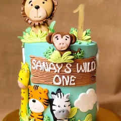 A "Wild One" jungle theme cake for a first birthday. This cake is decorated with adorable, friendly fondant animals like a lion, tiger, monkey, and giraffe.