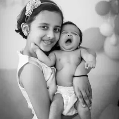 A big sister holds her yawning newborn sibling. Black and white photography beautifully captures the raw, unscripted moments of family life.