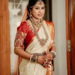 A full-length portrait of the bride in her beautiful off-white and red silk saree, showcasing her complete traditional Muhurtham look.