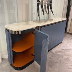 This elegant sideboard features a white marble top and a body finished in a dusty blue Duco paint. The fluted, curved doors and chrome accents give it a sophisticated, Art Deco feel.