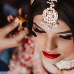 Final touches. Applying mascara to complete the dramatic eye makeup, which perfectly balances the statement red lip for a truly unforgettable bridal look.