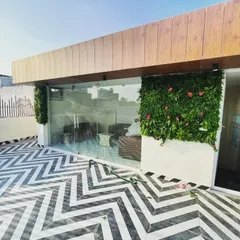 The entrance to a terrace lounge area, framed by artificial green walls with pink flowers. The bold black-and-white chevron floor tiling provides a striking contrast.