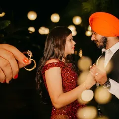 A creative shot focusing on the engagement ring held in the foreground, with the couple dancing romantically in the softly lit background.