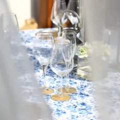 A dreamy, light-filled table setting with delicate glassware and a blue floral runner. This artistic shot captures the romantic and enchanting atmosphere we strive to create.