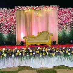 This stunning reception stage features a massive wall of pink and white flowers, creating a luxurious and romantic backdrop. The stage is lined with a mix of colorful blooms, perfect for a grand celebration.
