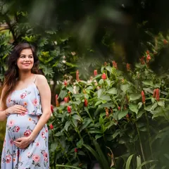 The maternal glow is real. This outdoor maternity portrait captures an expecting mother in a beautiful floral dress, surrounded by lush greenery and flowers. The natural setting complements the natural beauty of pregnancy.