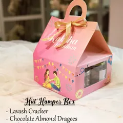 The Hut Hamper Box for Raksha Bandhan is a cute and compact gift. It contains a pack of lavash crackers, chocolate almond dragees, a jar of red velvet cookies, and a resin rakhi.