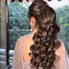 A glamorous high ponytail with voluminous curls, perfect for a reception or cocktail party. The hair is wrapped at the base for a sleek finish, and the highlights add beautiful dimension to the curls.