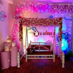 This is a modern and stylish baby shower setup, perfect for an indoor space. It features a silver-coated jhula decorated with pink and white flowers, a balloon arch in shades of pink, and cute props like a snowman and cloud cutouts with soft lighting.