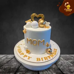 A simple and elegant birthday cake for "Mom." The clean white design is accented with gold lettering, hearts, and spheres, making for a classy and loving tribute.
