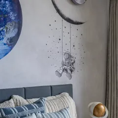 The wall art in this kids' room brings the universe indoors, with a crescent moon, a dreamy astronaut, and a unique astronaut sculpture lamp that adds playful wonder.