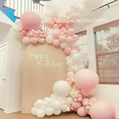 This beautiful organic balloon garland in pastel pink and white flows down the side of a neutral-toned arched backdrop. It's a perfect example of soft, modern, and minimalist party decor.