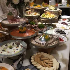 A multi-tiered buffet display with a variety of Mediterranean and international dishes. Using wooden logs and slate platters for presentation adds a rustic yet sophisticated touch to this house party setup.