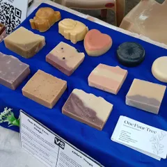 A display of my diverse soap collection at a local market. You can see various shapes, sizes, and natural colorants, from the heart-shaped 'Juliet' to the dark Activated Charcoal soap and fun animal shapes for kids.