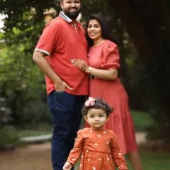 A classic family standing portrait in the park. The little girl takes center stage, showcasing her personality while her parents stand lovingly behind her.