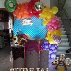 This candy-themed birthday party features a bright, colorful balloon garland over a polka-dot backdrop. The plinths are designed to look like ice cream cones and candy jars, perfect for a sweet celebration.