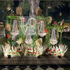 This boho-glam photo backdrop with a 'LOVE' neon sign is perfect for a cocktail night. The mix of chandeliers, pampas grass, and red florals creates a unique and highly Instagrammable spot.
