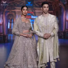 A breathtaking bridal couple on the runway. The bride's golden lehenga with zardosi work is perfectly matched with the groom's sophisticated gold raw silk sherwani, embodying modern opulence.
