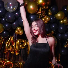 The party isn't just about decor, it's about the feeling. Here, the birthday girl enjoys the atmosphere I created with a black and gold balloon wall, holding a glass and dancing the night away.