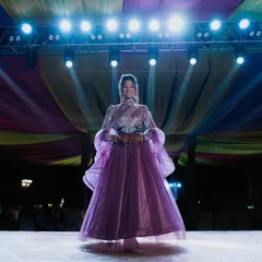 A stunning solo portrait of the bride on the sangeet stage. The dramatic stage lighting highlights her beautiful gown and confident presence.