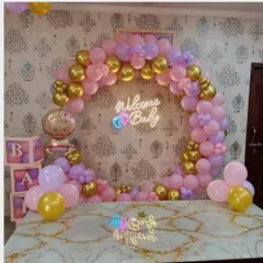 A beautiful "Welcome Baby" arch in shades of pink, purple, and gold. This setup includes a neon sign, 'BABY' blocks, and a baby girl foil balloon, perfect for a tabletop display.