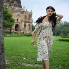 A candid walking shot that captures movement and personality. The composition uses the tree to frame her, with the Lodi Garden tomb creating a classic backdrop.