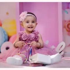 A happy smile from a baby girl during her candy-themed photoshoot. The background features giant ice cream cones and macarons, creating a sweet and colorful setting.
