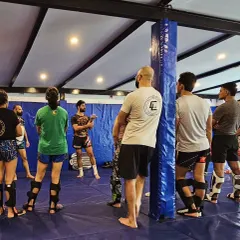 Students listening as the coach details the finer points of a technique. Everyone is geared up in shin guards, ready to drill what they've just learned.
