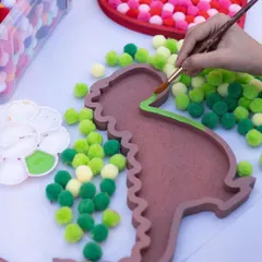 Get ready to make the cutest dinosaur ever! This pom-pom dino kit starts with painting the outline of the tray, then filling it with soft green pom-poms. It's a great sensory activity for little hands.