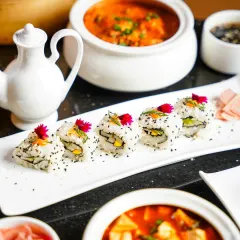 A close-up of delicate sushi rolls garnished with edible flowers, set against a backdrop of flavorful Asian curries. This shot highlights the artistry and freshness of the ingredients.