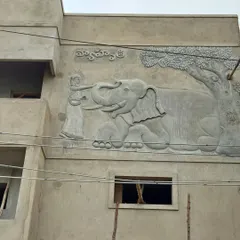 This large exterior mural shows an elephant being blessed, with the house name sculpted in Telugu above it. This is a beautiful example of combining animal art with personalized elements for a home's facade.