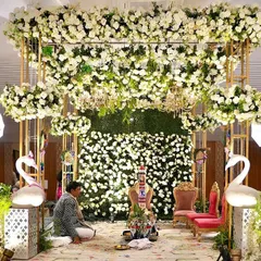 A breathtaking floral mandap for a day wedding. The structure was adorned with thousands of white flowers and lush greenery, with elegant swans and chandeliers adding a touch of fairytale magic.