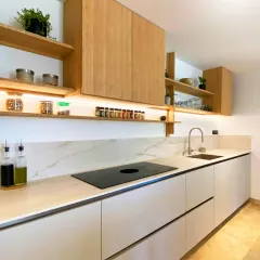 A minimalist kitchen design featuring light wood upper cabinets and open shelving, paired with sleek white base units and a marble-patterned backsplash.