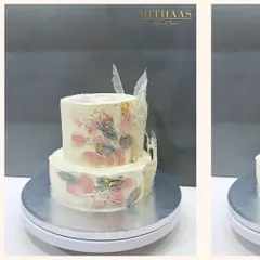 This two-tiered cake showcases a painterly effect, achieved by hand-painting the cocoa butter frosting with natural tints from berries. The abstract strokes of pink and grey, highlighted with gold leaf, create a unique, artistic finish.