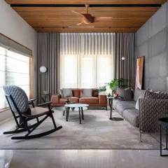 A living room from our Faizal Residence project, designed for comfort and conversation. We combined a plush patterned sofa with a classic leather couch and a modern rocking chair, all set against a backdrop of exposed concrete and warm wood ceilings to create a space that is both sophisticated and welcoming.