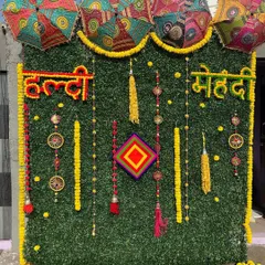 A wider view of the green wall setup, showing how the combination of yellow marigold garlands and colorful props stands out. This type of backdrop is great for outdoor or well-lit indoor spaces.