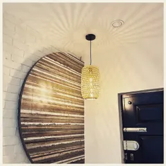 This cylindrical woven pendant light casts a stunning starburst pattern on the ceiling. We paired it with a large, circular wooden wall art piece to create a composition of natural textures and warm, ambient light.