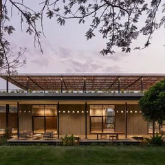 The facade of 'The Earth' at dusk, where the warm interior lighting glows through the large glass windows, highlighting the building's strong horizontal lines and natural material palette.