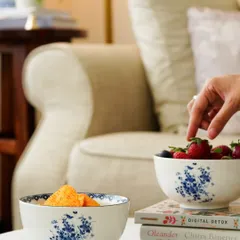 A lifestyle shot of ceramic bowls filled with snacks on a coffee table. A hand reaching for a strawberry adds a human touch, making the scene feel natural and lived-in.