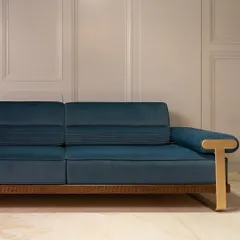 A comfortable and classy couch designed for ultimate relaxation. This piece features a rich blue velvety fabric, a sturdy wooden base with woven details, and distinctive T-shaped brass handles for a touch of modern sophistication.