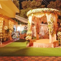 A beautiful mandap for an evening wedding on a lawn, decorated with peach drapes, white flowers, and fairy lights for a warm, glowing effect.