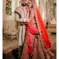 A classic wedding day portrait of the couple. The bride's stunning red lehenga and the groom's coordinated attire are captured in a moment of loving embrace.