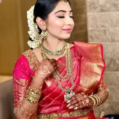 This bride's look is all about traditional elegance. The makeup features golden eyeshadow and a defined lip, complementing her layered gold necklaces and bright pink Kanjivaram saree.